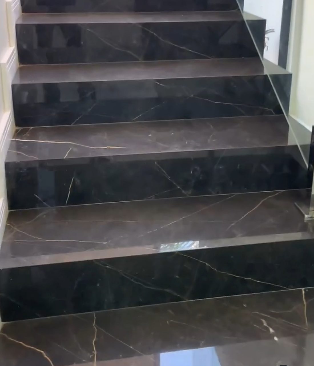Escada em tom escuro com veios claros e guarda-corpo de vidro